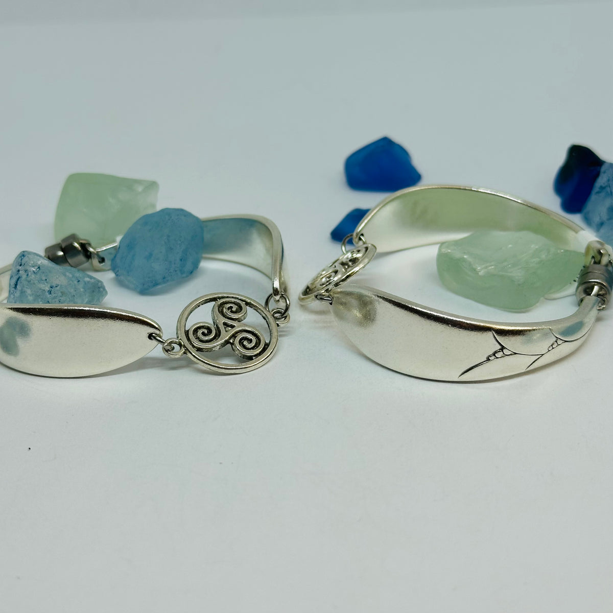 Close-up of two Lady Hamilton 1932 vintage spoon bracelets: one with a triskele charm, one with an etched spoon bowl.