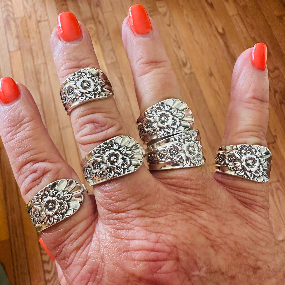 Floral vintage silverware rings worn on several fingers against a wood floor.