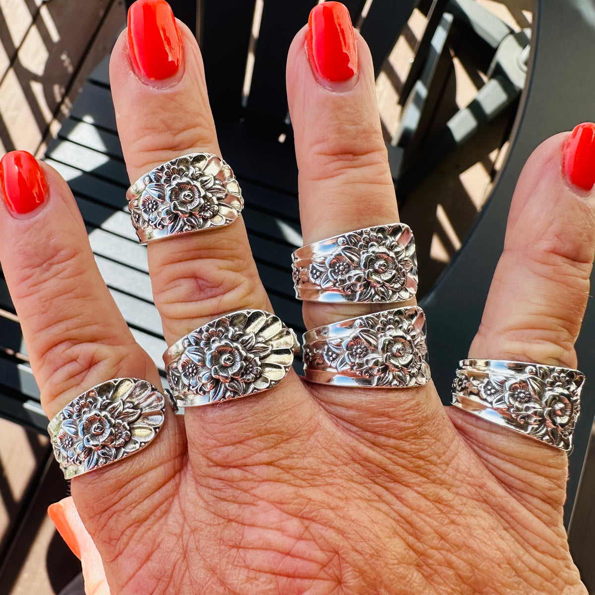 Floral vintage silverware rings worn on several fingers against a dark outdoor railing.
